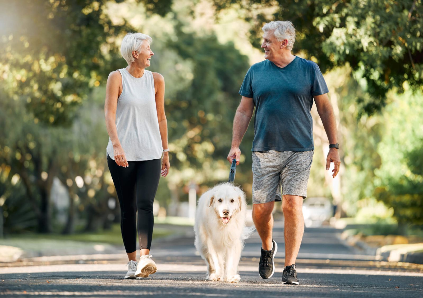 Older woman and man walking dog outside, looking happy