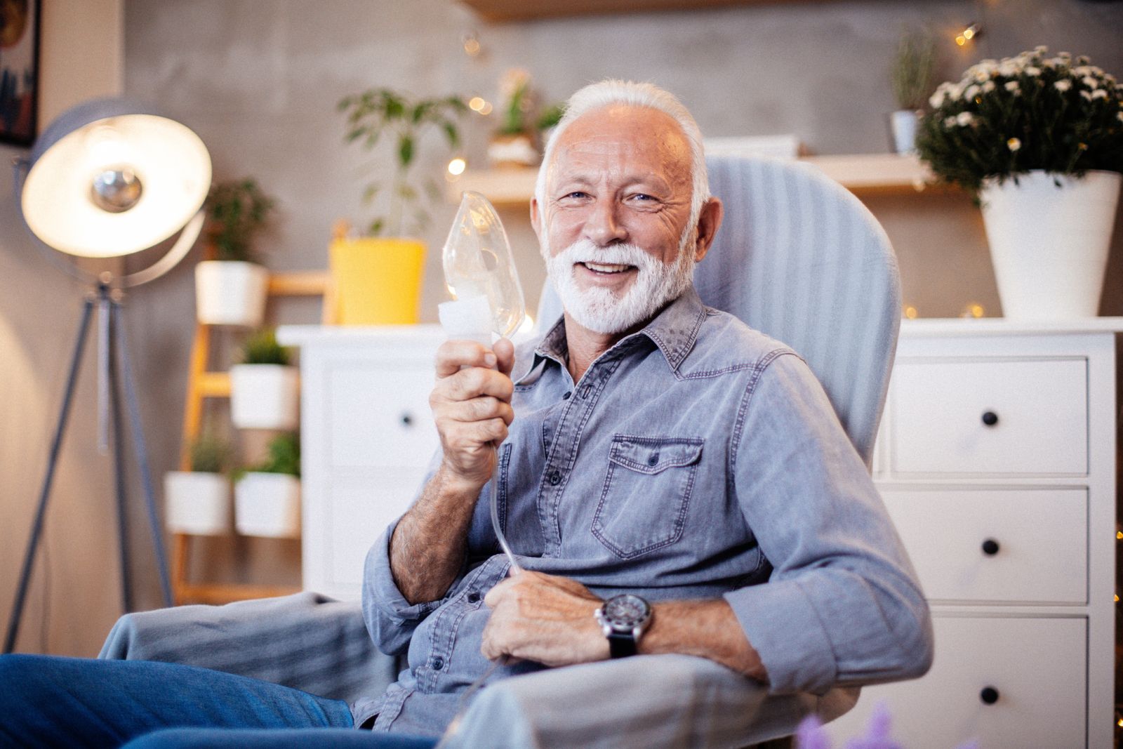 Smiling senior man sitting in chair with a respiratory mask in his hand